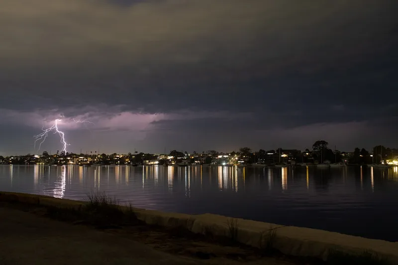 Lightning strikes over a waterfront town at night.